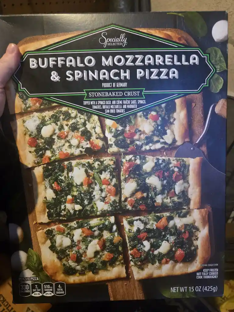 A hand holds a frozen pizza box labeled 'Buffalo Mozzarella & Spinach Pizza', which claims to be a 'Product of Germany' and…