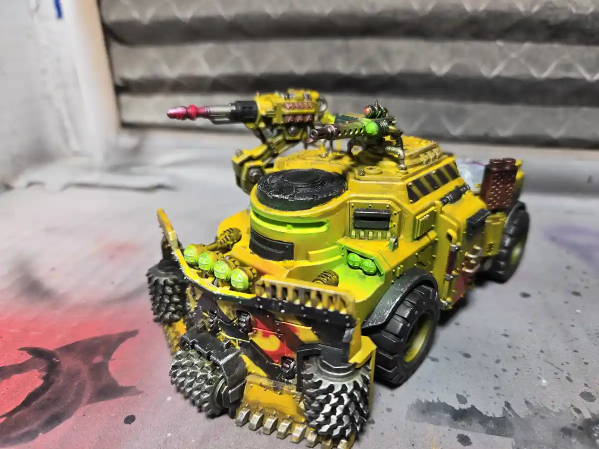 A heavily detailed, custom-painted yellow and green miniature tank model with multiple weapons and spiked treads sits on a…