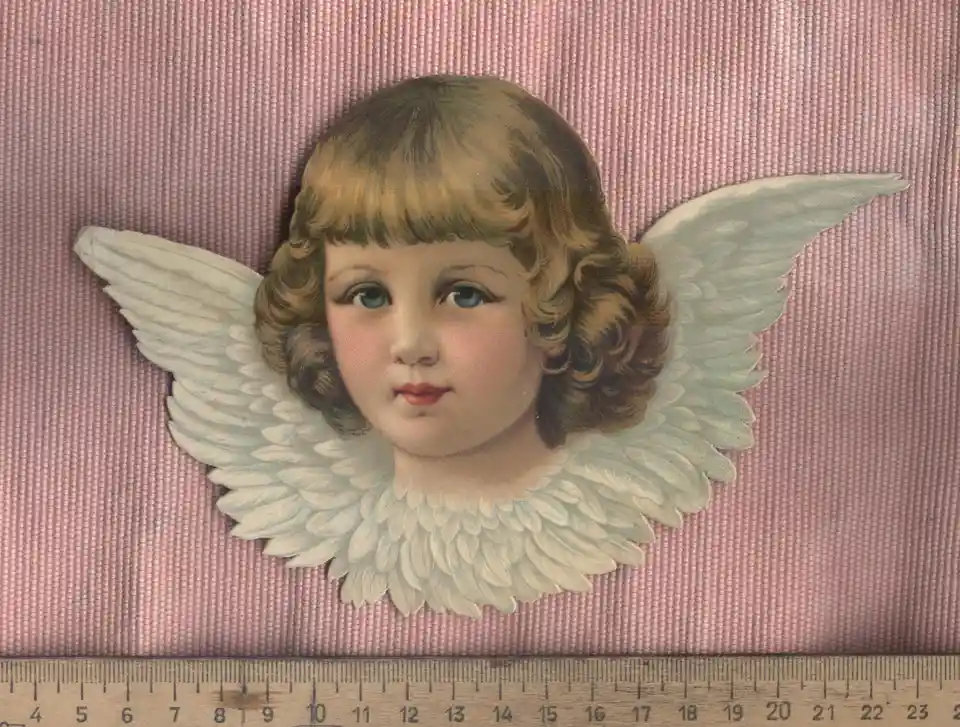 A vintage paper cutout of a cherubic angel with curly blonde hair and large white feathered wings is displayed against a…