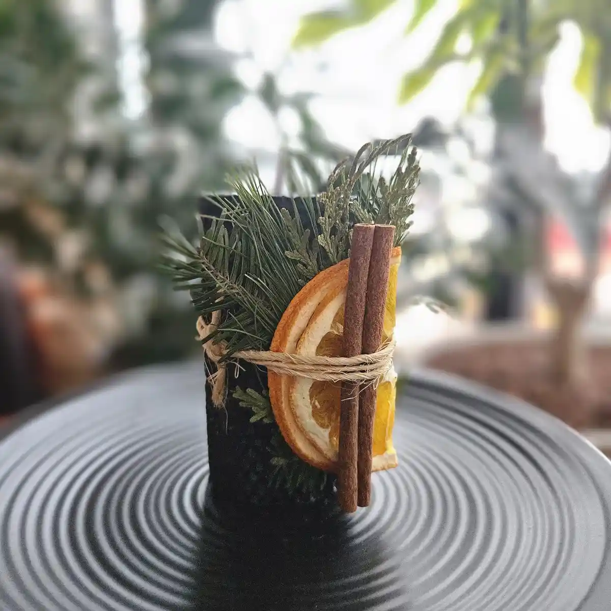 A black cylindrical object, resembling a candle, is decorated with dried orange slices, cinnamon sticks, and pine sprigs…