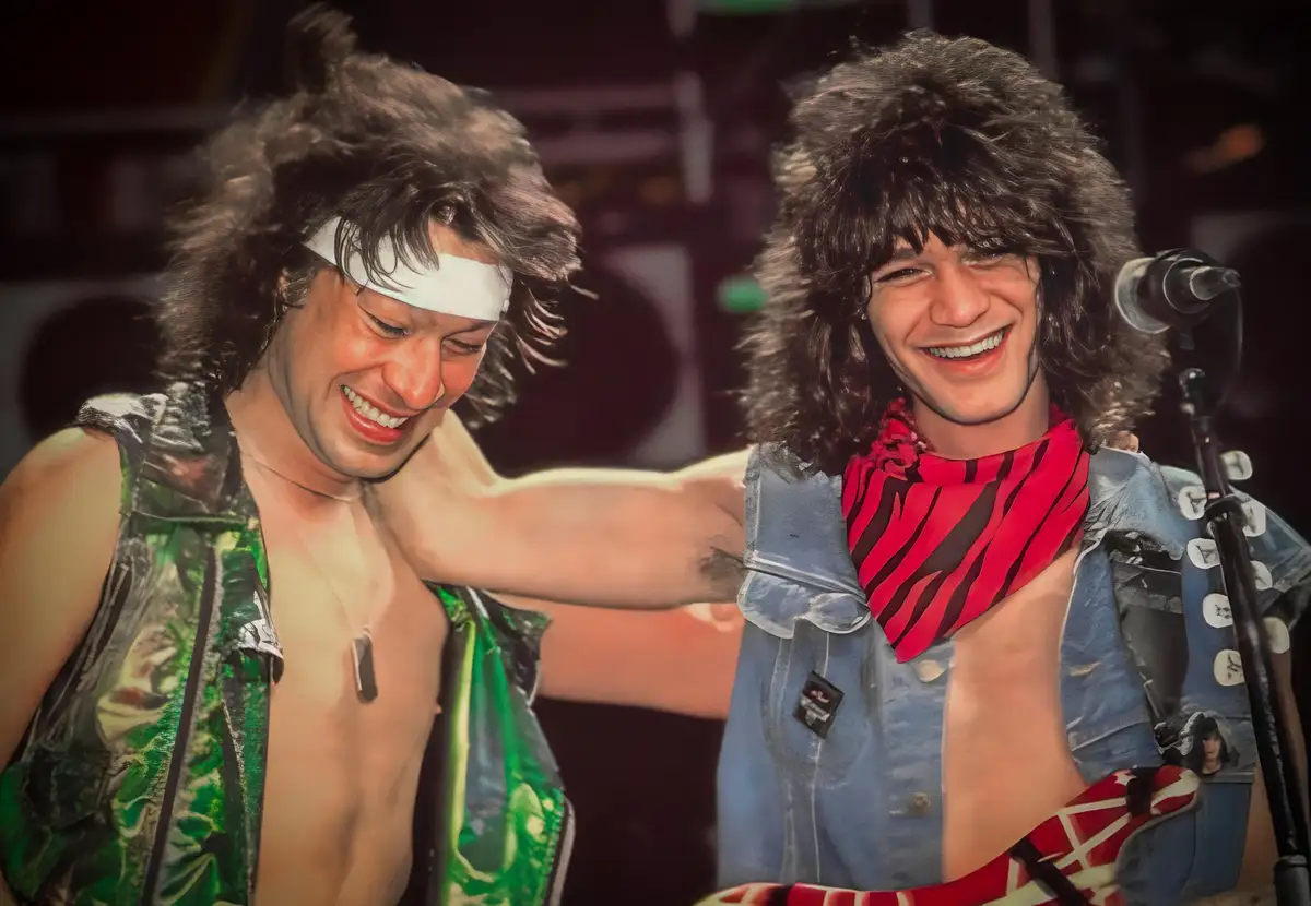 Two men with long, curly hair and 1980s rock star attire are smiling and laughing while on stage. One wears a green…