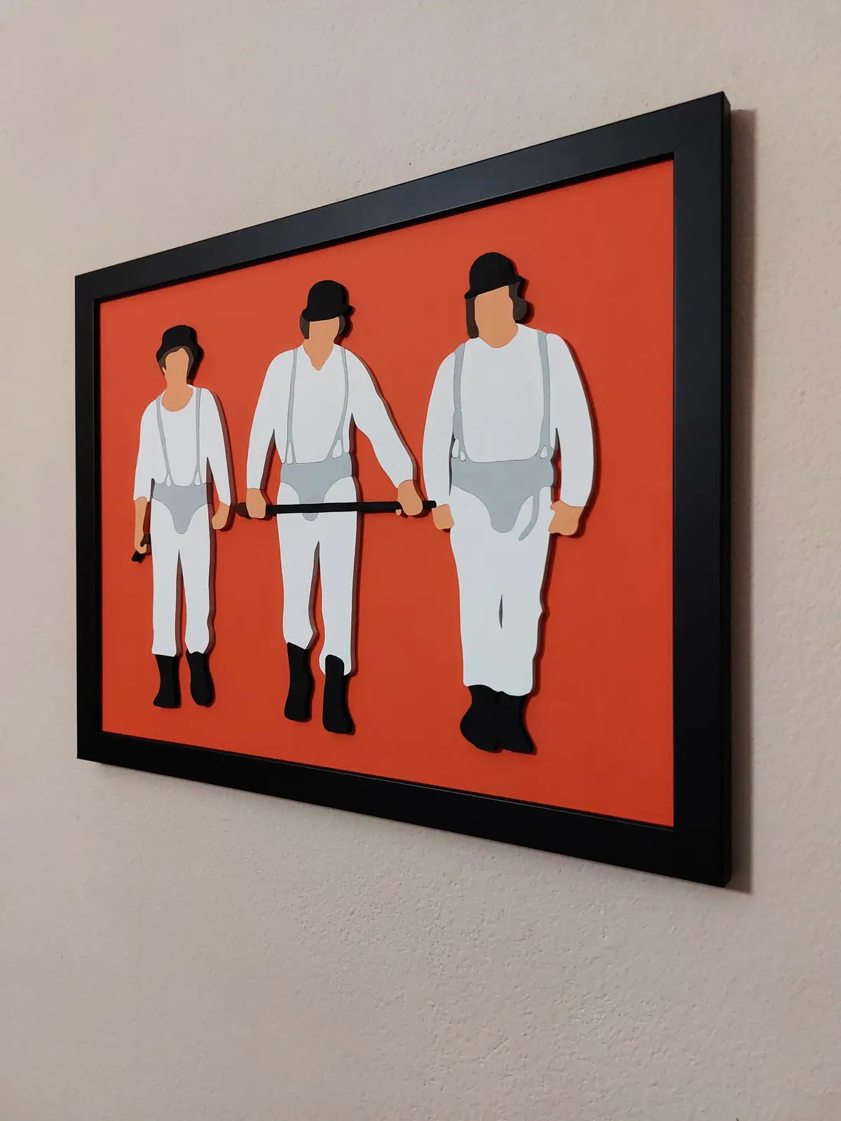 A framed artwork on a wall depicts three stylized, faceless figures in white outfits with suspenders and black bowler hats…