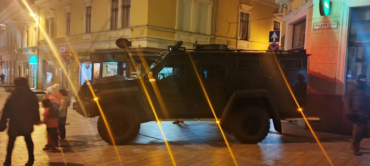 A large, black armored vehicle is parked on a city street at night, illuminated by bright yellow streetlights that create…