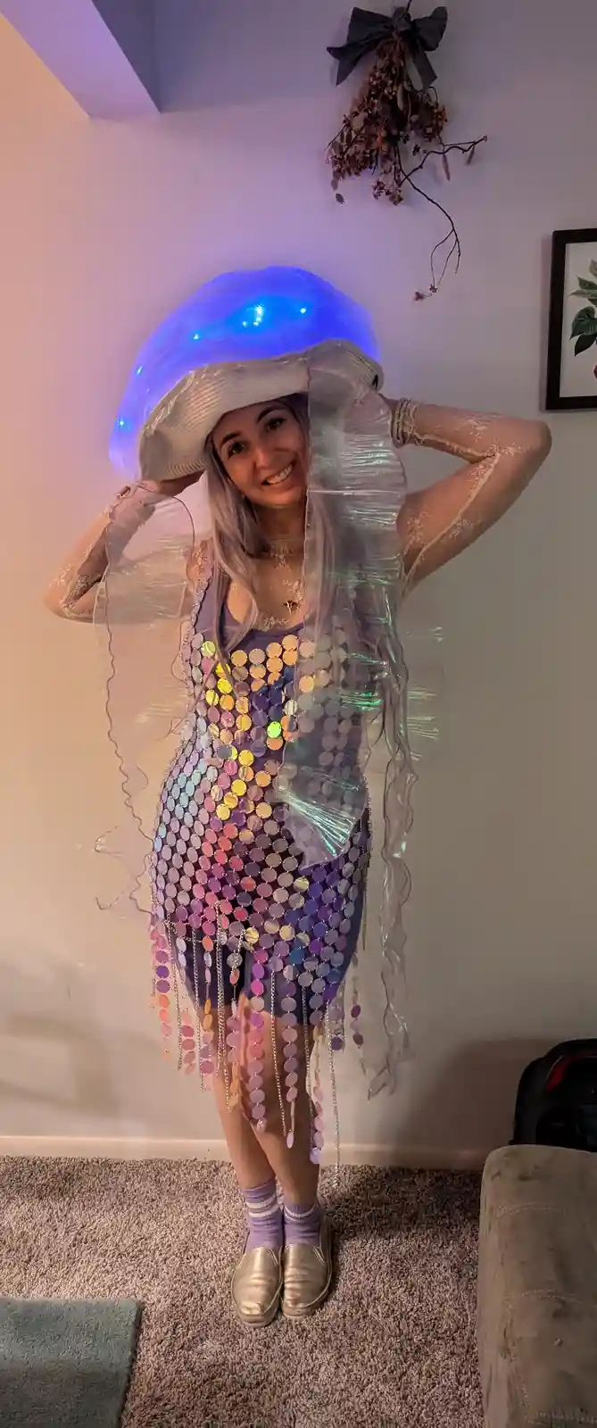 A person in a homemade jellyfish costume stands indoors, smiling at the camera. The costume features a large, translucent…