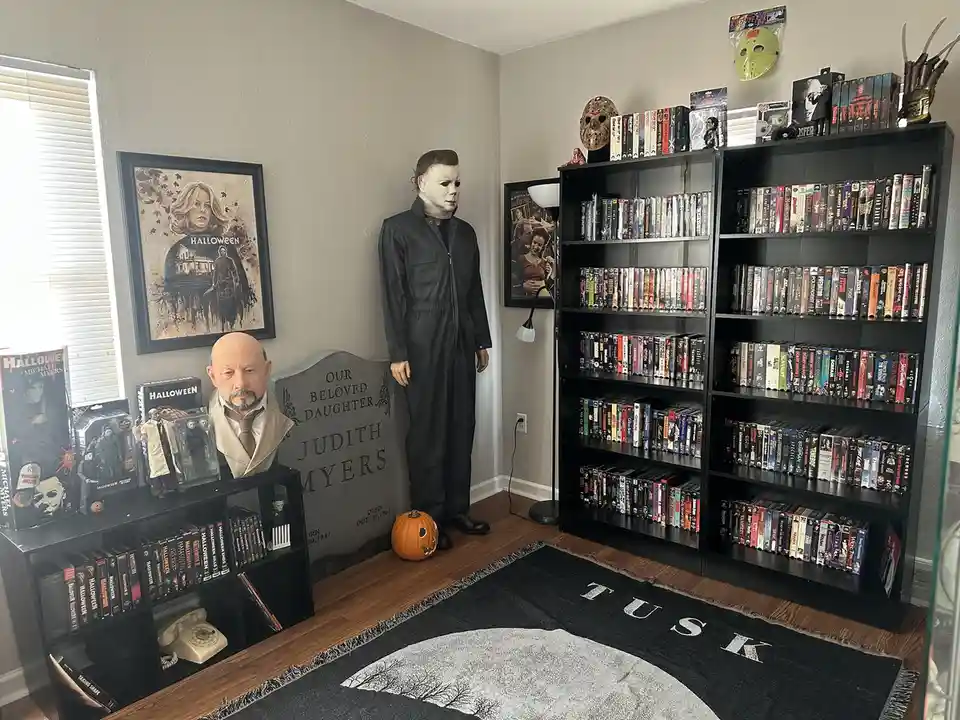 A room filled with horror movie memorabilia, including a full-sized Michael Myers mannequin, a tombstone for Judith Myers, a…