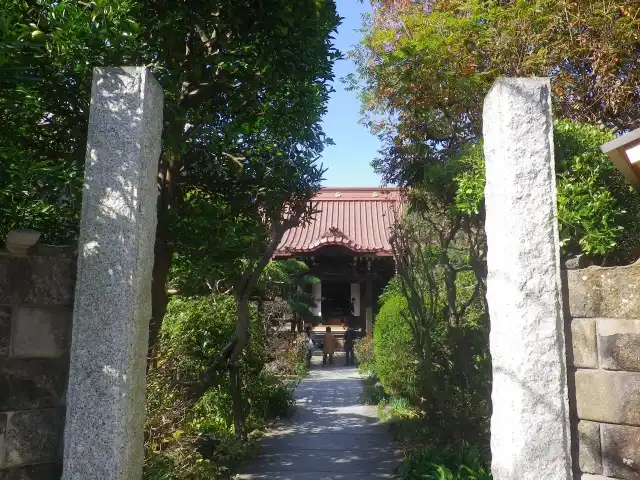 a serene garden path framed by two tall stone pillars leads to a traditional Japanese-style building with a red-tiled roof…