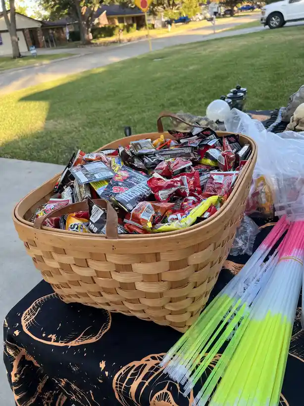 A large woven basket overflowing with assorted Halloween candy sits on a table covered with a black and orange…