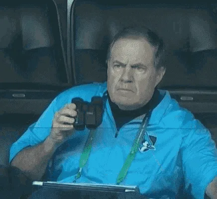 A man in a blue polo shirt and lanyard sits in stadium seats, holding binoculars. In the top row, he looks annoyed and…