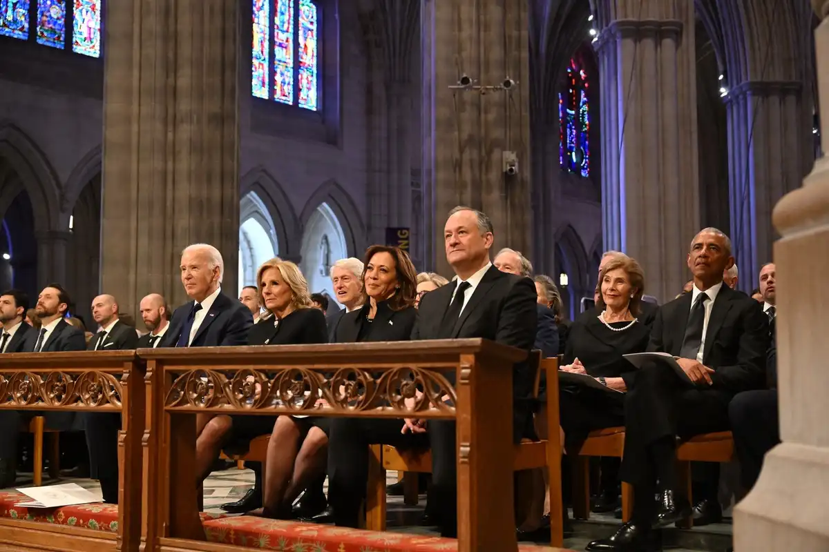 A photo of several prominent political figures, including Joe Biden, Kamala Harris, and Barack Obama, seated in a church pew…