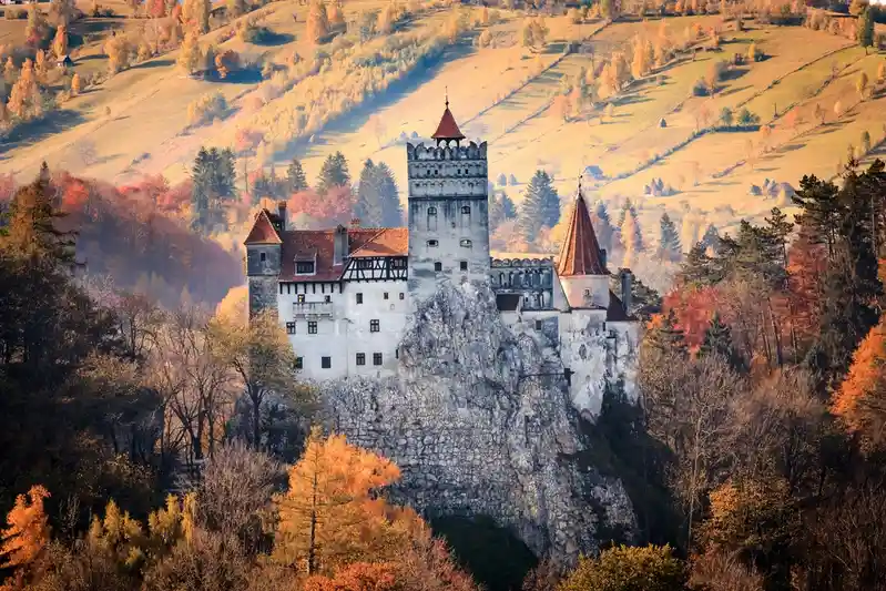 a picturesque view of a stone castle with red-tiled roofs perched on a rocky outcrop, surrounded by rolling hills covered in…