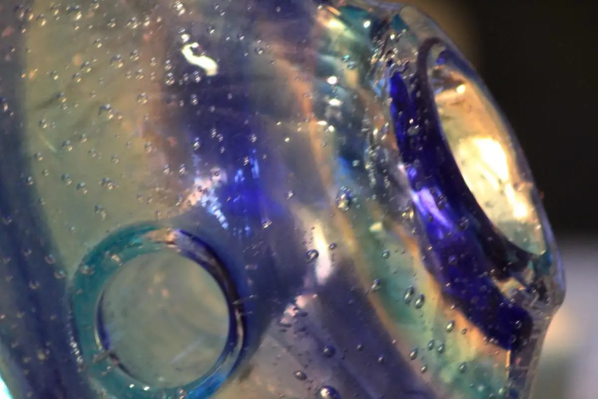 A close-up photo of a translucent, iridescent glass bottle with bubbles and two circular indentations resembling eyes…