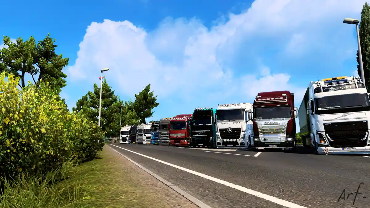 A row of colorful, modern semi-trucks parked side-by-side on a paved road under a bright blue sky with fluffy clouds. Lush…