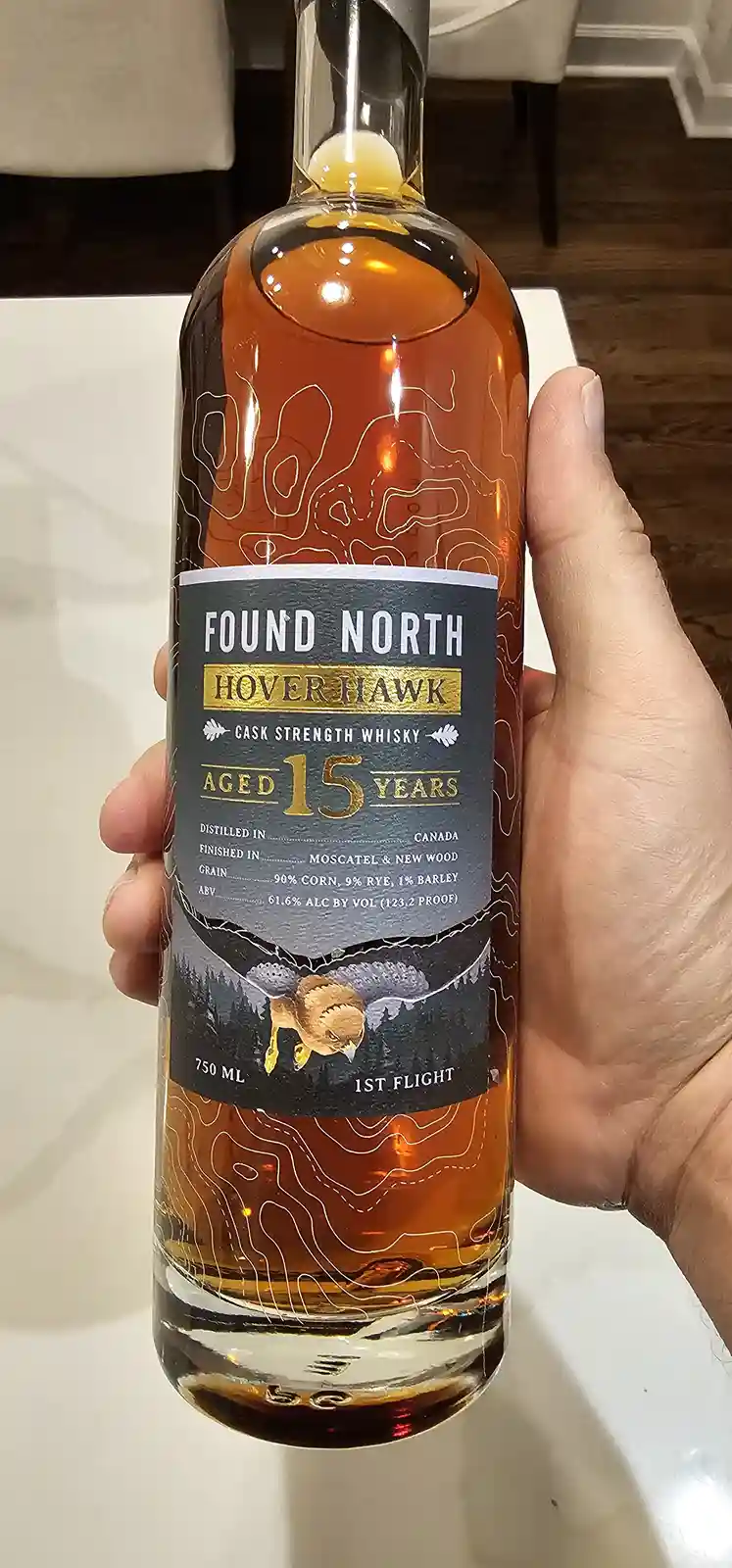 A hand holds a bottle of Found North Hover Hawk 15-year-old cask strength whisky, featuring a label with topographic lines…