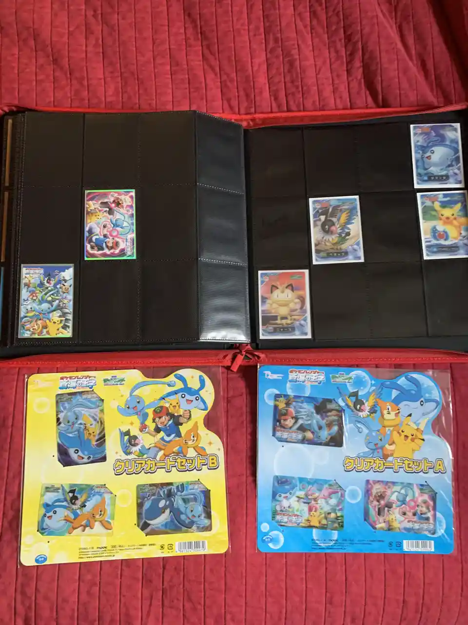 An open black Pokemon card binder with several cards inserted into pockets, sitting on a red fabric surface. Below the…