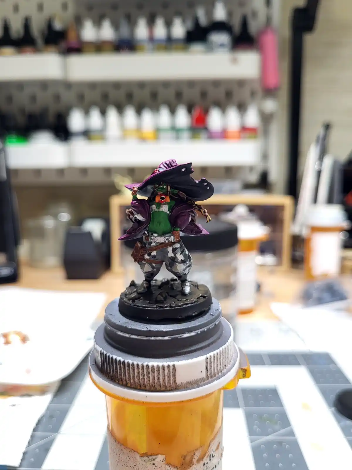 A painted fantasy miniature figure, resembling a green-skinned wizard or rogue in a purple cloak and wide-brimmed hat…
