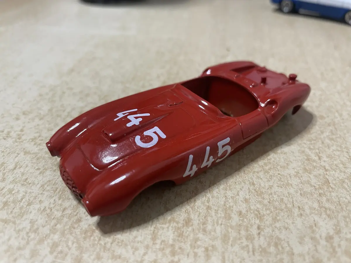 A red toy race car body with the number '445' painted on its side and hood, sitting on a speckled beige countertop. The car…