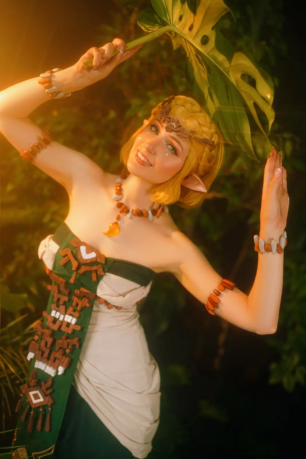 A person in a detailed cosplay of Zelda from The Legend of Zelda: Tears of the Kingdom stands in a jungle setting, holding a…