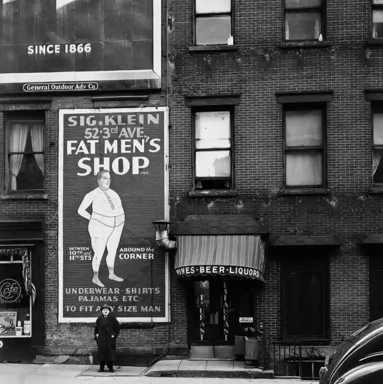 A black-and-white photograph shows a large vintage billboard advertising 'Sig. Klein, Fat Men's Shop' on 52nd Street…