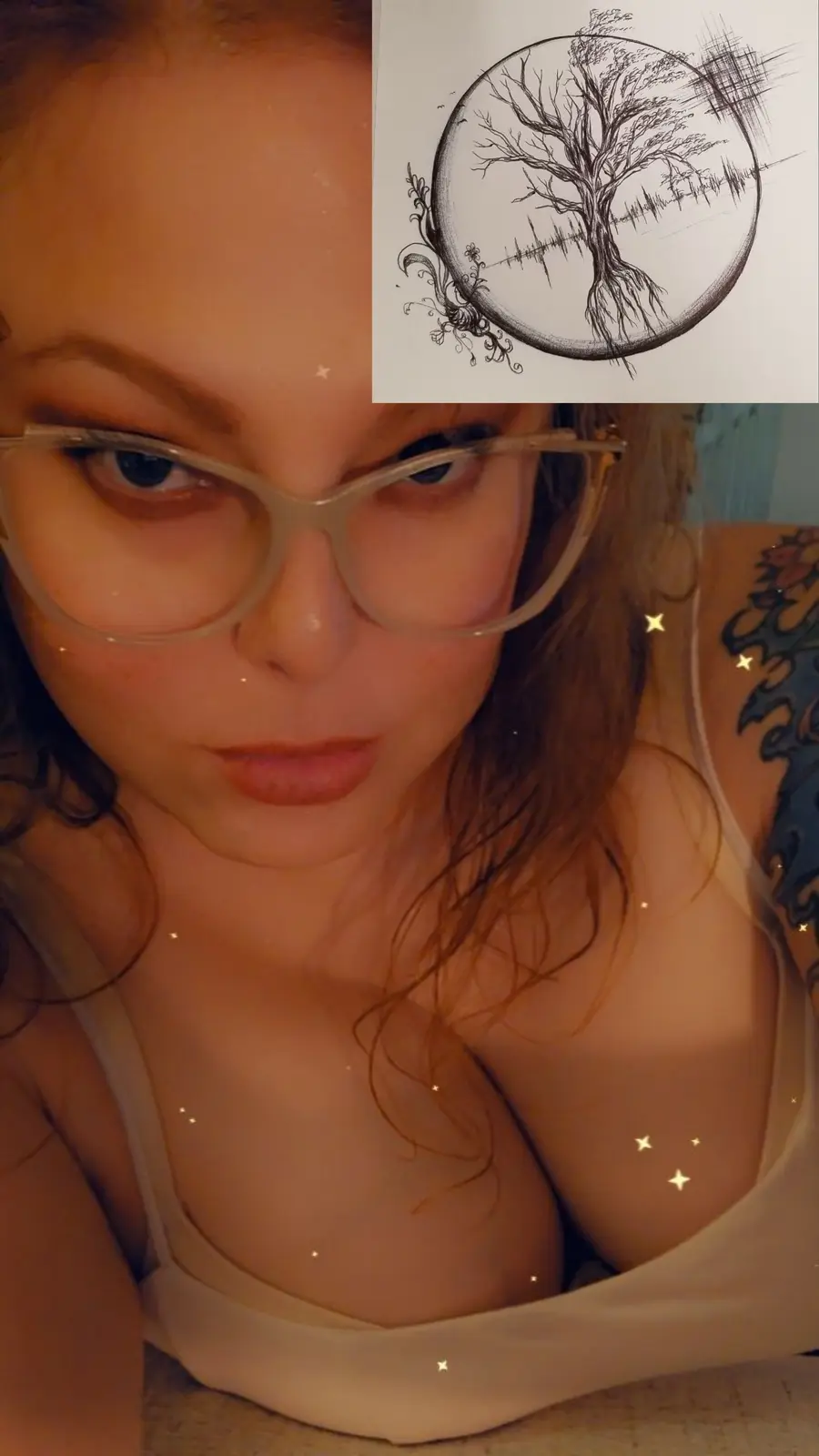 A selfie of a woman with glasses and a visible tattoo on her shoulder, overlaid with a sketch of a tree of life design. The…