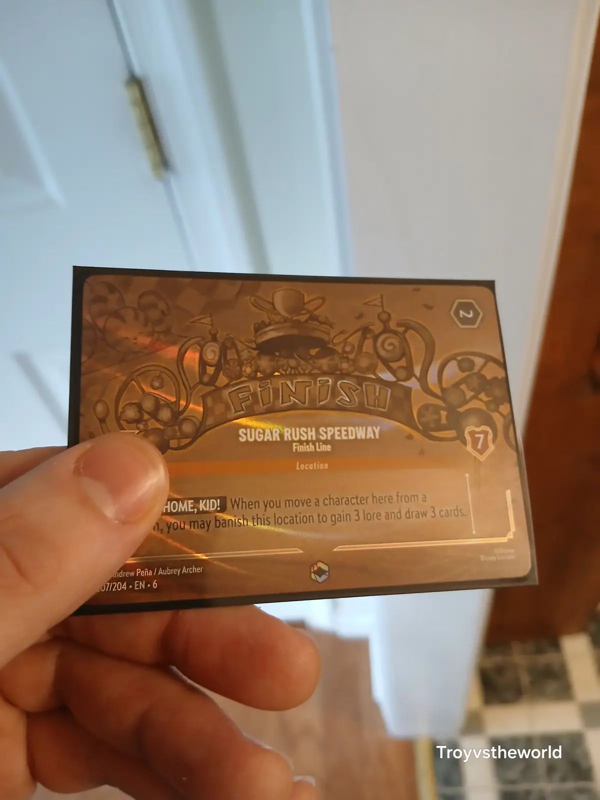 A hand holds a Disney Lorcana trading card titled 'Sugar Rush Speedway' with 'Finish' at the top. The card's text reads…