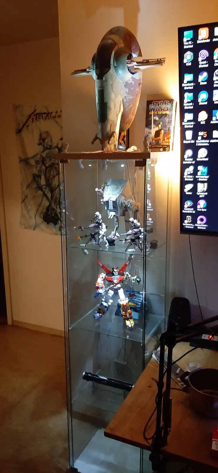 A glass display case holds a collection of sci-fi toys including a Star Wars AT-AT walker, a red and white robot, and a…