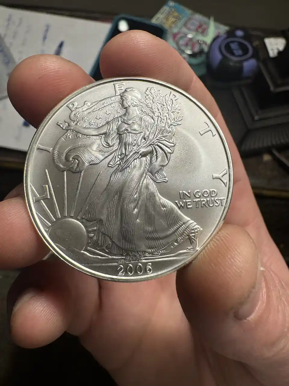 A close-up photo shows a person's hand holding a 2006 American Silver Eagle coin, which features the Walking Liberty design…
