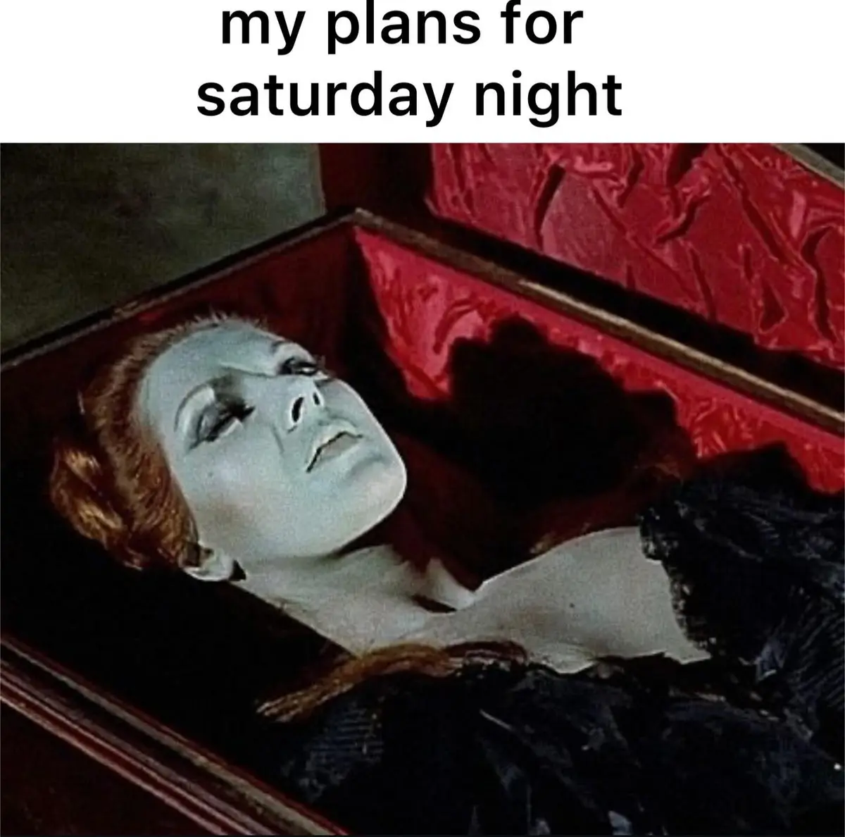 A still image from a horror film shows a pale woman with red hair lying in an open coffin lined with red fabric. She wears a…