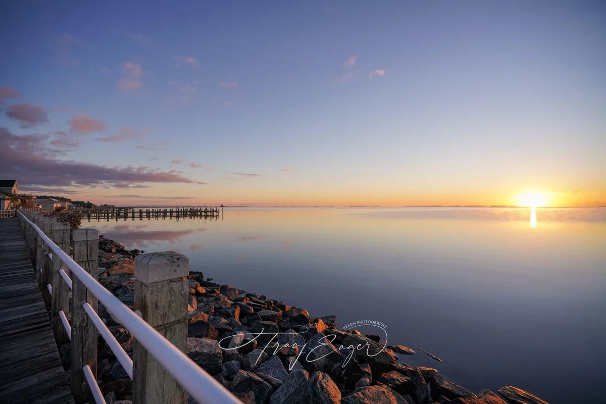 A serene sunset photograph shows a calm body of water with the sun setting on the horizon, casting orange and pink hues…