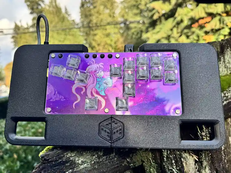 A custom mechanical keyboard with a purple galaxy-themed plate featuring an anime-style character is shown outdoors on a…
