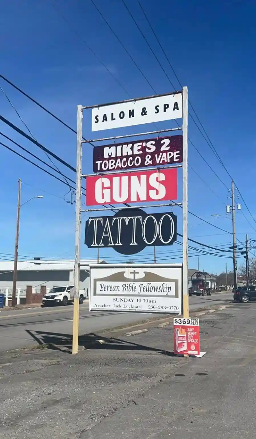 A tall, multi-tiered roadside sign under a clear blue sky advertises a variety of services including a salon & spa, tobacco…