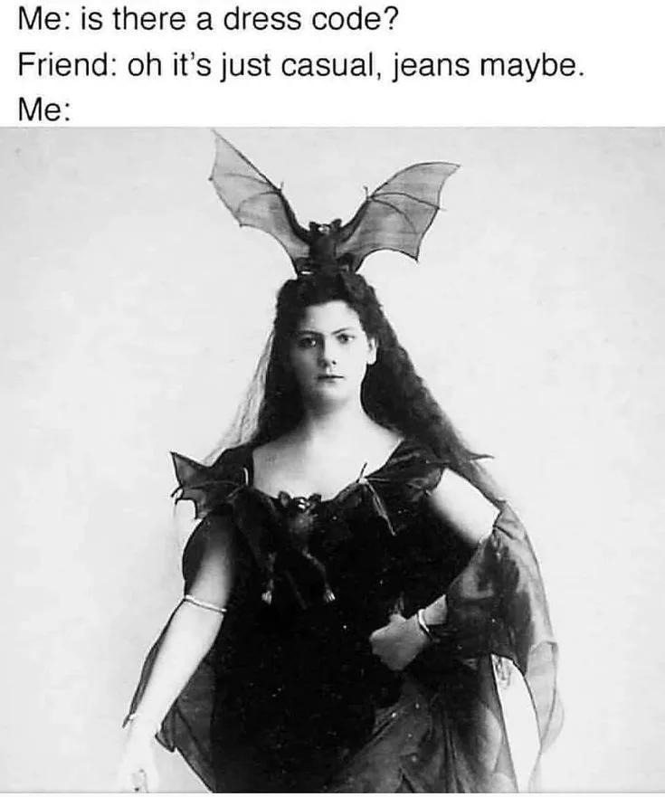 A black-and-white vintage photograph shows a woman in a dark, elaborate costume with bat wings on her head and bat-like…
