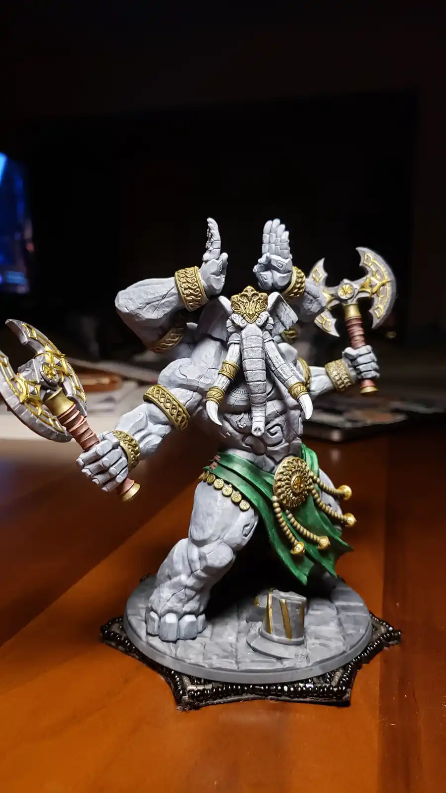 A heavily detailed, painted miniature figurine of a muscular, grey-skinned stone-like god with multiple arms, holding two…