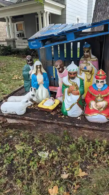 A backyard nativity scene with plastic figurines of Mary, Joseph, baby Jesus, and the three wise men, all painted with black…