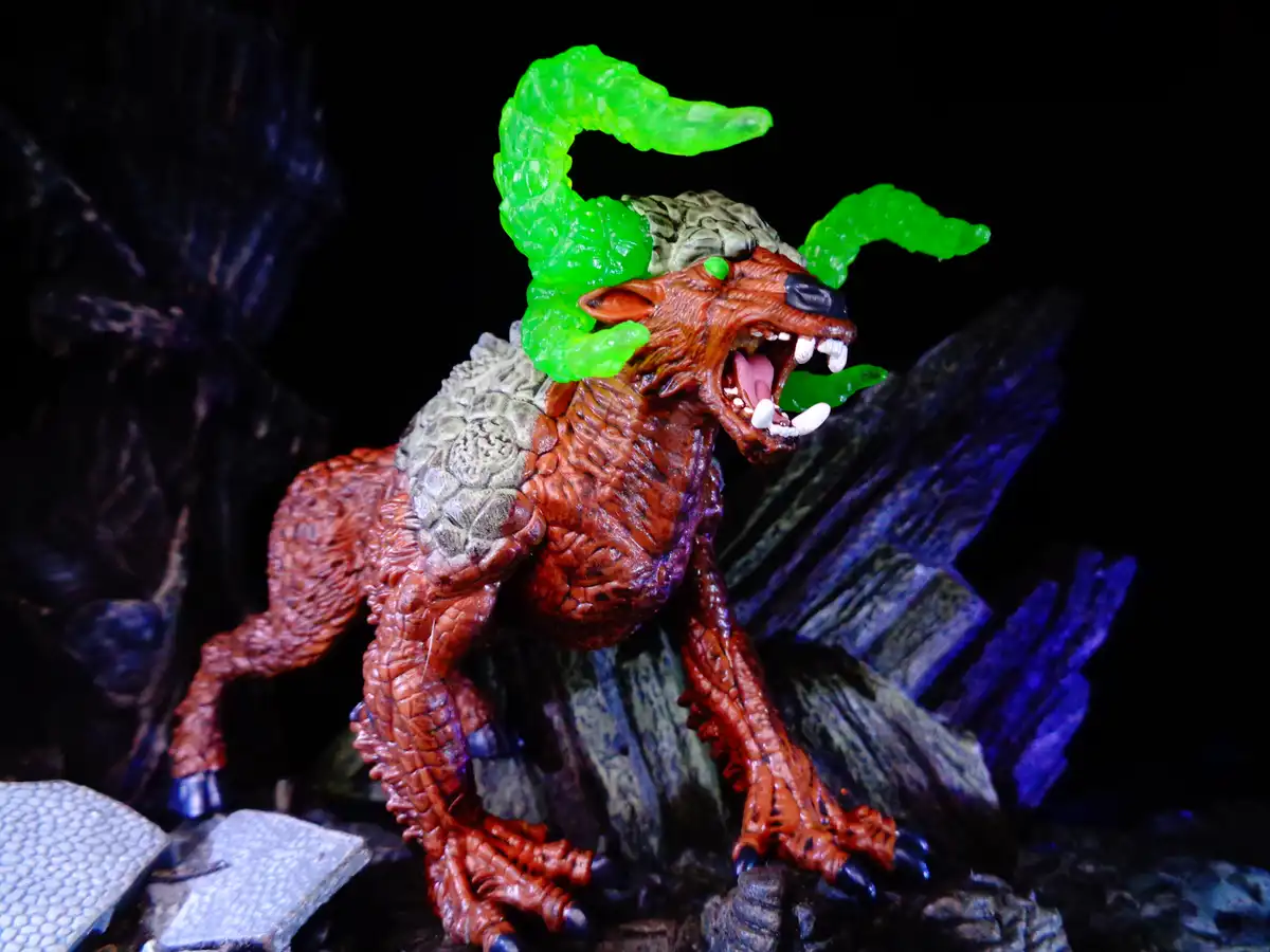 A detailed action figure of a monstrous, red-skinned beast with glowing green horns and a snarling expression, posed on…