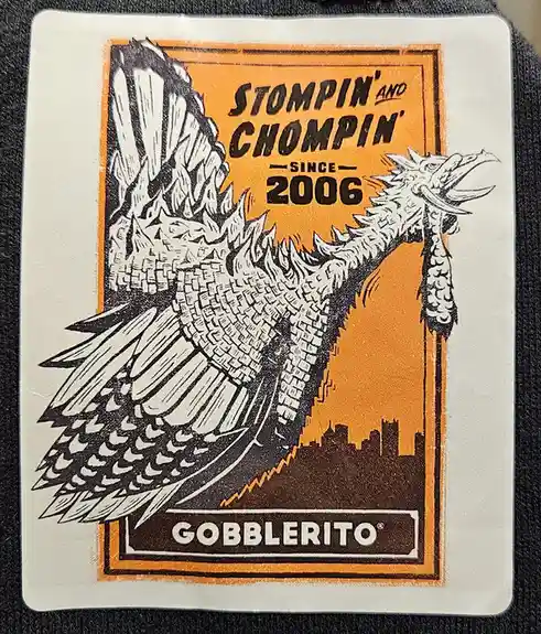 A sticker features a stylized, winged, reptilian creature with a spiked back and tail, resembling a dragon or dinosaur, set…