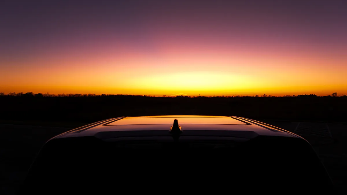 A car's roof is silhouetted against a vibrant sunset with orange, pink, and purple hues. The overlaid text reads 'i'm not…