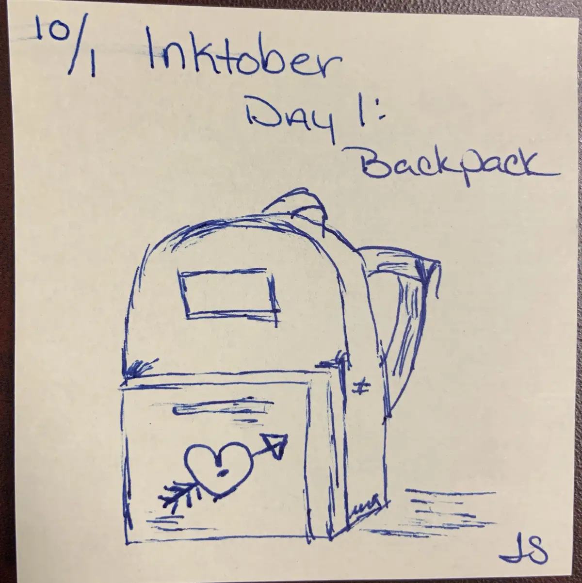 A simple blue ink drawing on a sticky note shows a backpack with a heart pierced by an arrow on its front pocket. Above the…