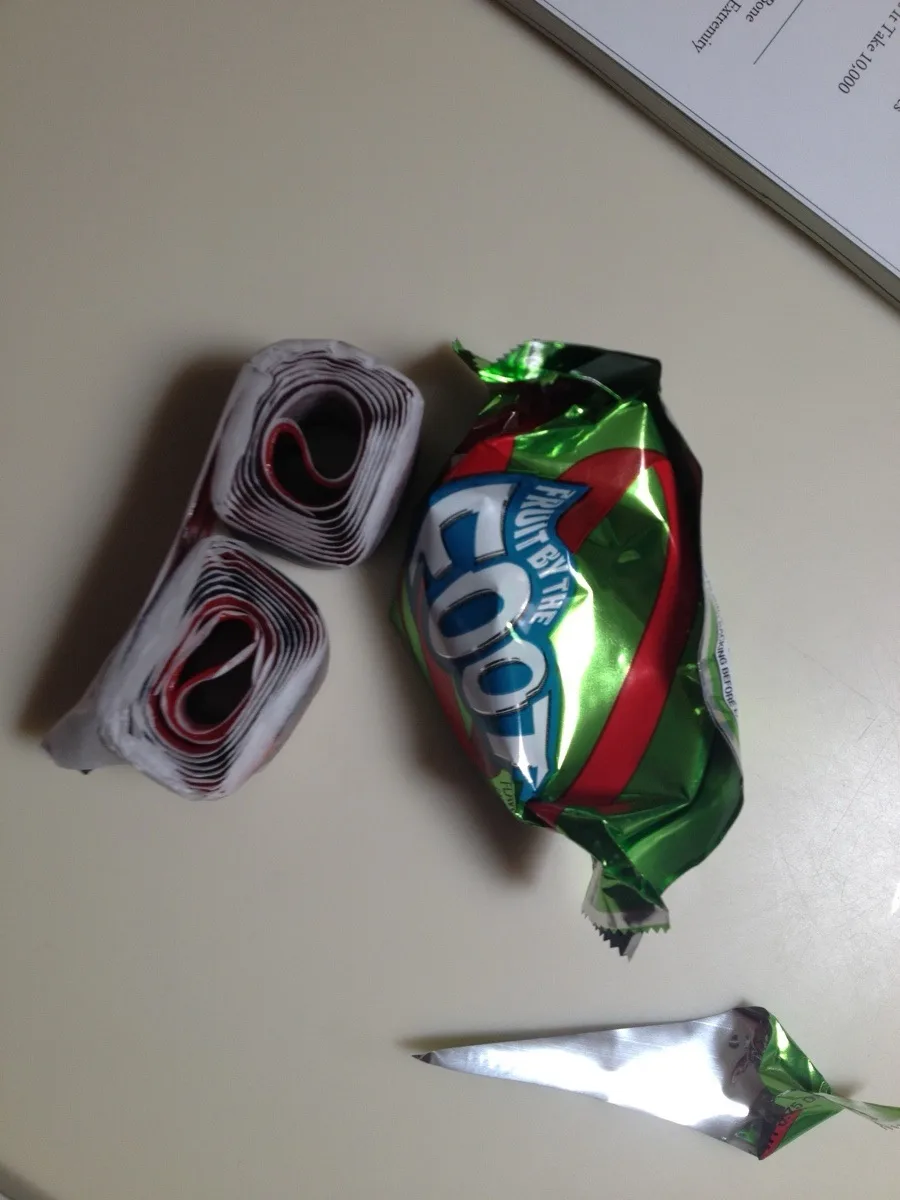 A crumpled green, red, and silver wrapper of Fruit by the Foot candy sits next to two rolled-up portions of the same snack…
