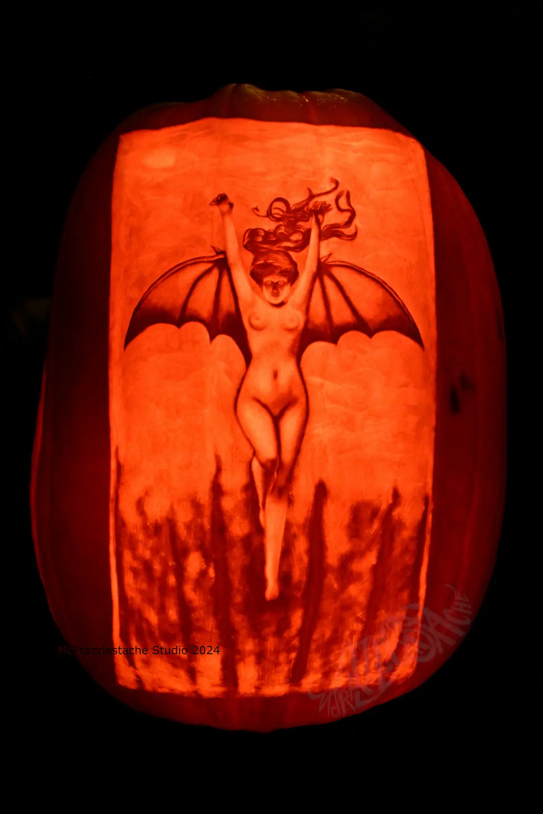 A large, intricately carved pumpkin illuminated from within, casting an orange glow. The carving depicts a nude, winged…