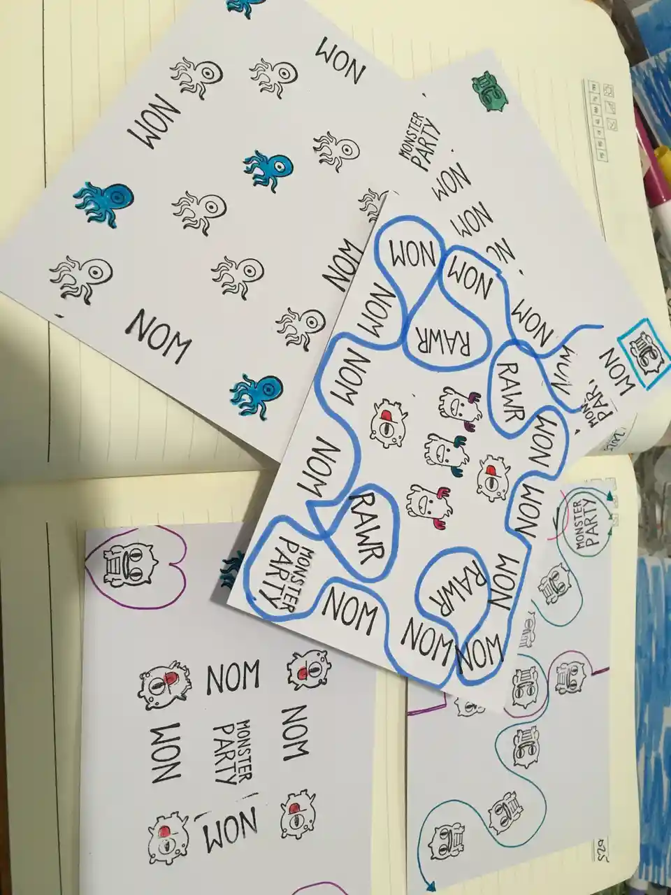 Several hand-drawn sheets on lined notebook paper show cartoon monsters with the words 'NOM' and 'RAWR' written next to…