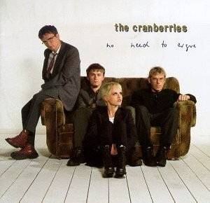 An album cover featuring four band members of The Cranberries sitting on and around a worn brown couch against a plain white…