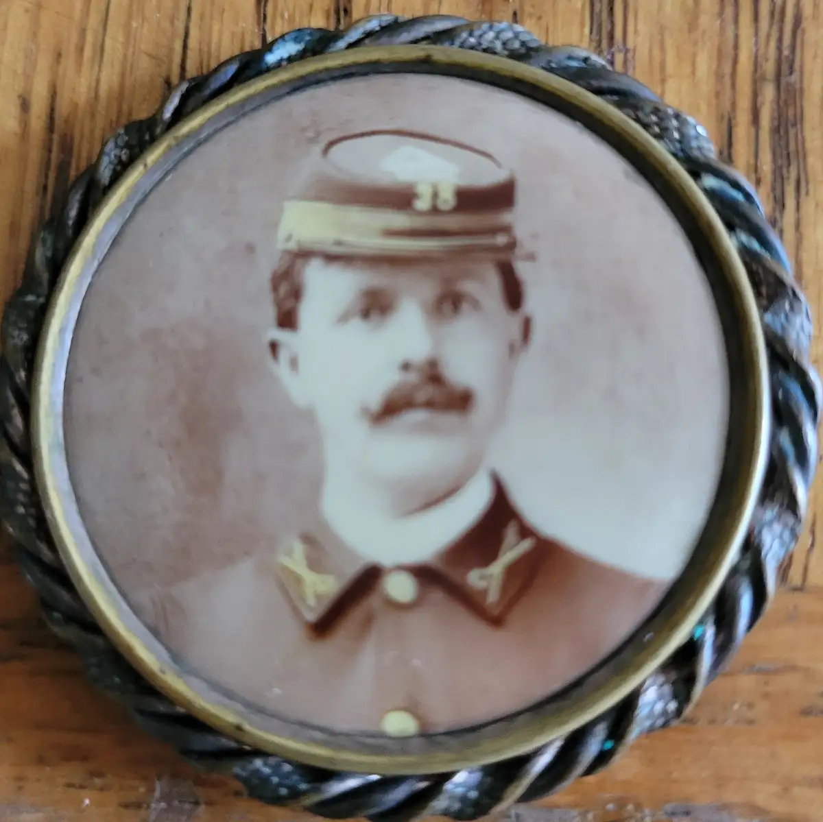 A vintage sepia-toned portrait of a mustachioed man in a military uniform with the number '38' on his cap, set within an…