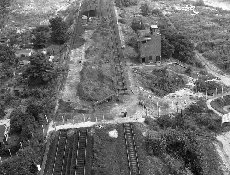 A black-and-white aerial photo shows a disused railway junction with overgrown tracks, a small tower, and scattered debris…