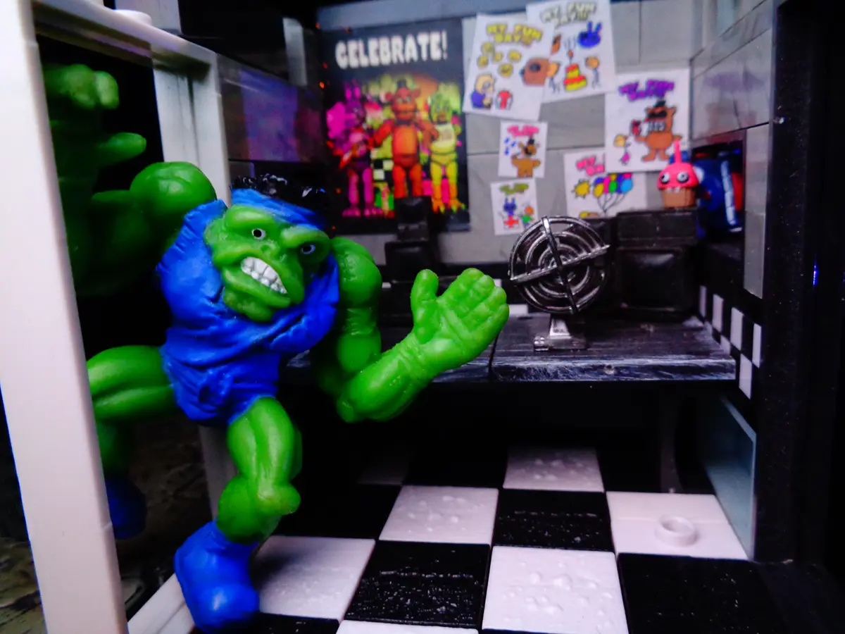 A green Hulk action figure in a blue outfit stands in a miniature room with a black-and-white checkered floor, appearing to…