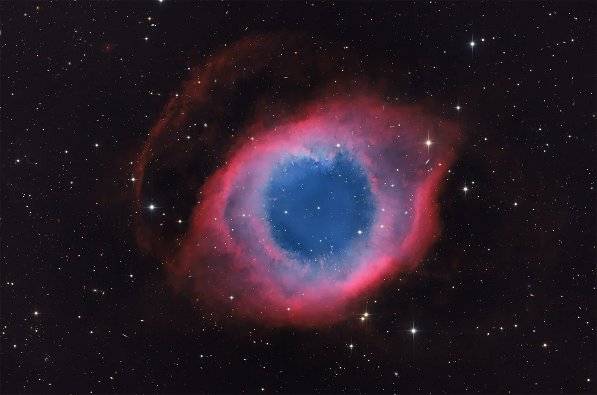 A cosmic image of the 'Eye of God' nebula, a celestial object resembling a human eye with a blue iris and red outer ring…