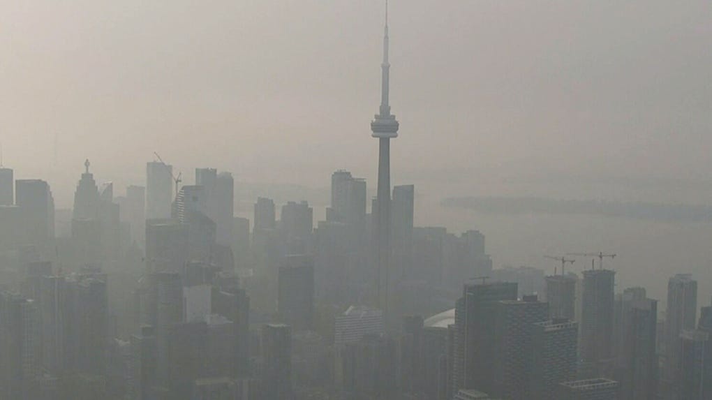 A hazy, smog-covered cityscape featuring the iconic CN Tower in Toronto, with skyscrapers barely visible through the thick…