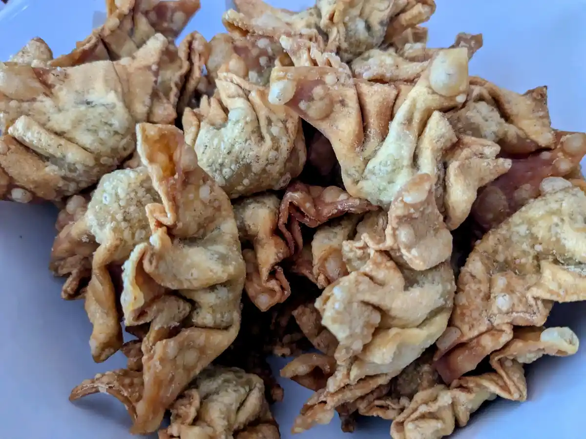 A close-up photo shows a pile of golden-brown, crispy fried wontons on a light blue plate. The wontons have a textured…