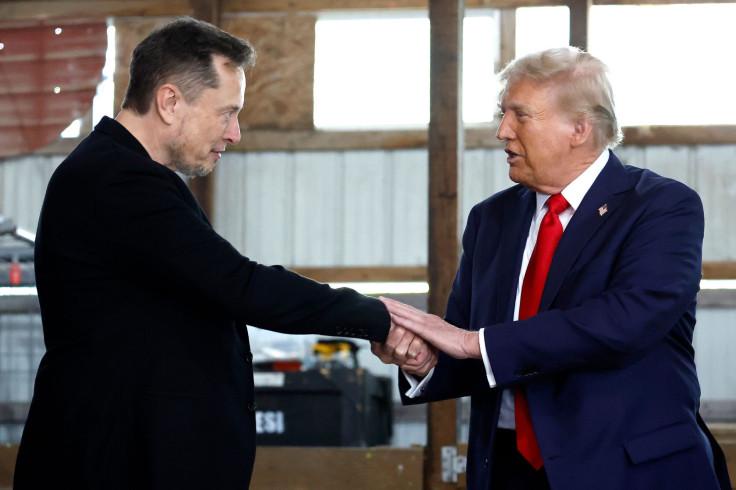 Two men, identified as Elon Musk and Donald Trump, are shaking hands in what appears to be a warehouse or industrial…