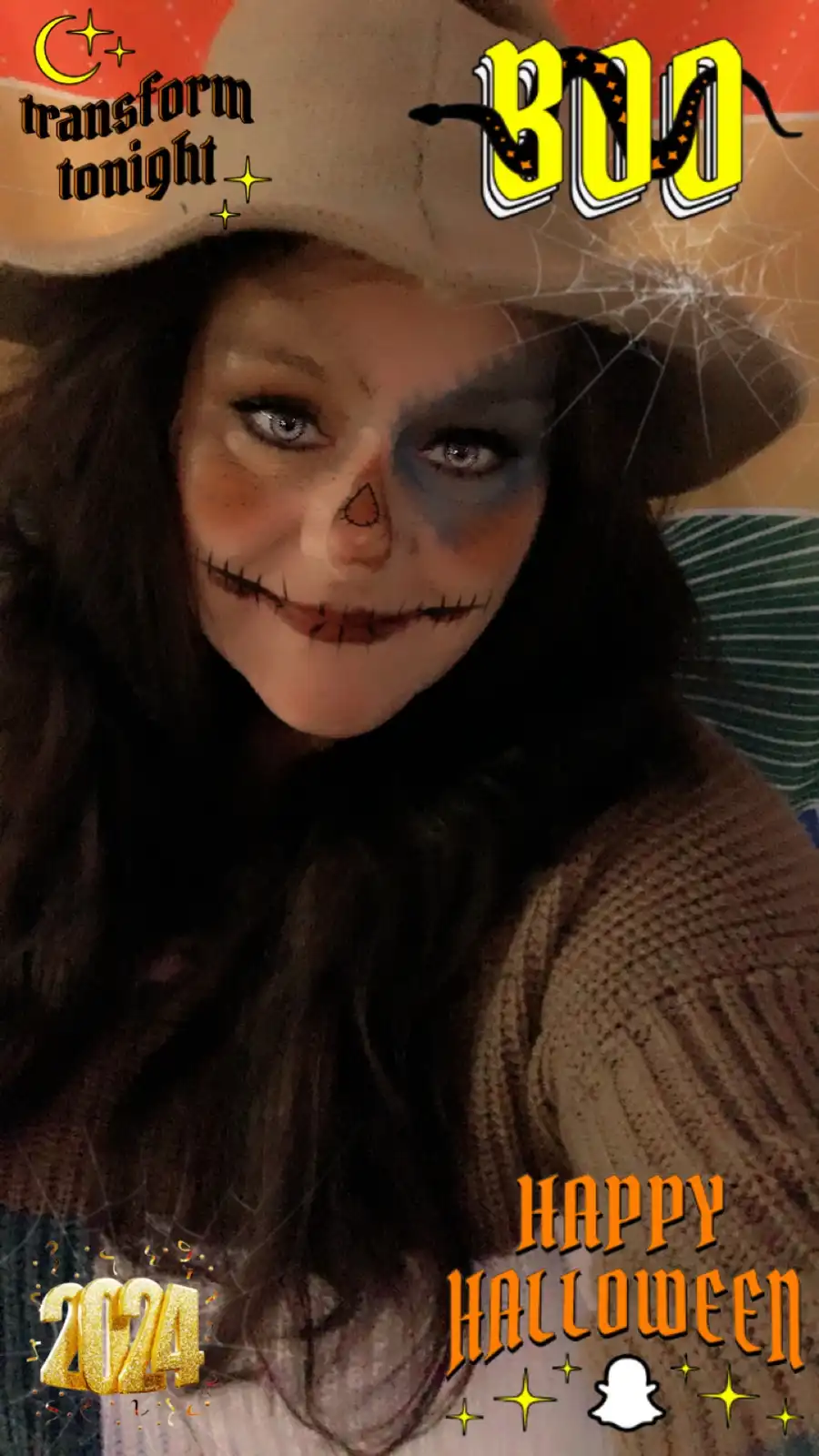 A person with long dark hair wears a cowboy hat and Halloween makeup resembling a stitched-up skull with one side painted…