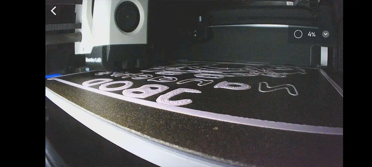 A close-up shot of a laser cutter in operation, engraving white, stylized letters onto a dark, textured surface. The…